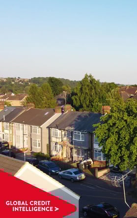 Vista aérea de un barrio suburbano bajo un cielo despejado, con una pancarta roja superpuesta en la que se lee "Global Credit Intelligence", que representa información sobre los mercados inmobiliario y crediticio.