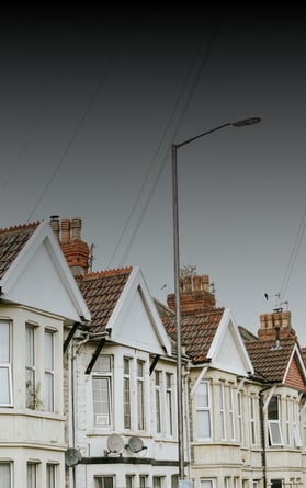 Una hilera de tradicionales casas adosadas británicas, que representan el mercado inmobiliario del Reino Unido. La imagen refleja temas como la valoración de la propiedad, las tendencias hipotecarias y la inversión inmobiliaria, con un cielo nublado como telón de fondo neutro.
