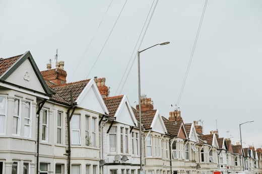 Una hilera de tradicionales casas adosadas británicas, que representan el mercado inmobiliario del Reino Unido. La imagen refleja temas como la valoración de la propiedad, las tendencias hipotecarias y la inversión inmobiliaria, con un cielo nublado como telón de fondo neutro.