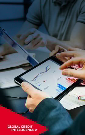 Equipo de empresarios revisando análisis en una tableta y un gráfico. Punto Chevron de Global Credit Intelligence en la esquina inferior izquierda superpuesto.