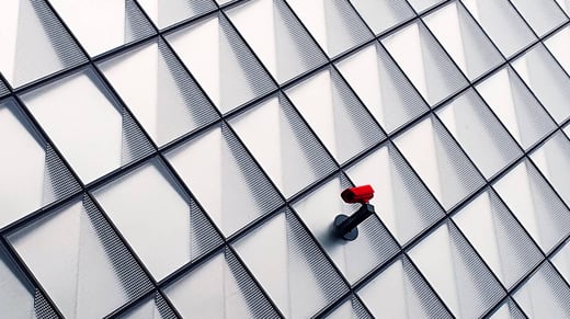 Una única cámara de vigilancia roja en la pared de azulejos de un edificio de oficinas