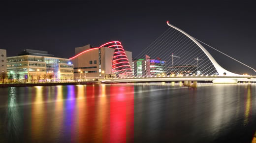 Foto nocturna del puente Samuel Beckett en Dublín bellamente iluminado por la luz de los edificios y farolas cercanos.
