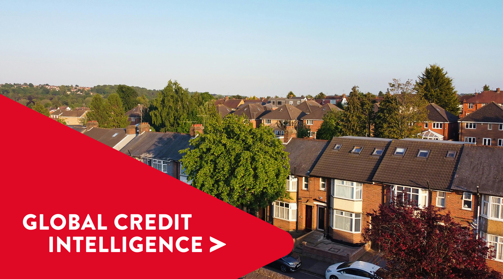 Vista aérea de un barrio suburbano bajo un cielo despejado, con una pancarta roja superpuesta en la que se lee "Global Credit Intelligence", que representa información sobre los mercados inmobiliario y crediticio.